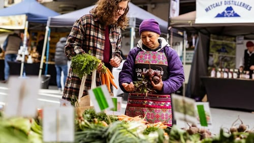 A bustling farmers market with people selecting fresh produce and interacting with vendors.