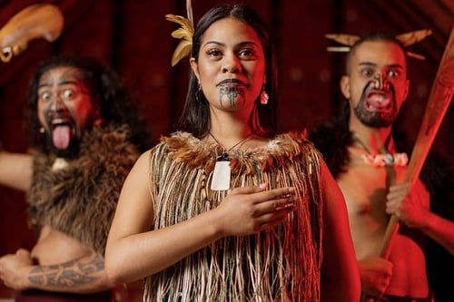 A group of Maori performers in traditional dress, dancing and singing on a stage.