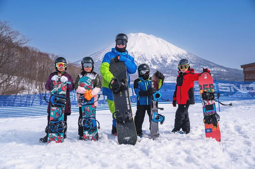 A group of children and one adult preparing to snowboard in Niseko