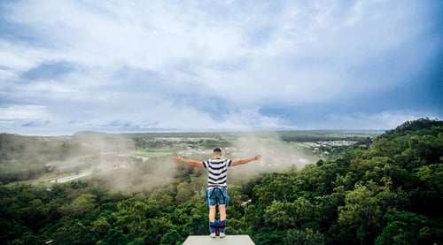 A person stands ready to bungee jump off a high platform, arms outstretched, overlooking a lush green valley with mist rolling in.