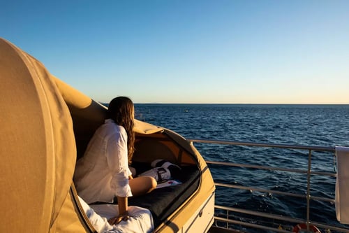 A serene ocean view from a boat, with a person sitting in a covered seat and gazing at the horizon.