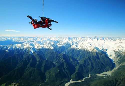 A skydiver freefalling over New Zealand_s picturesque landscape, with snow-capped mountains and blue skies in the background.