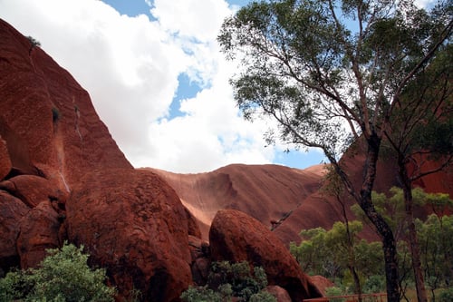 A stunning view of Uluru, the iconic red rock formation, surrounded by lush greenery under a partly cloudy sky.