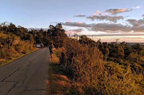 A tranquil road winding through Gooseberry Hill National Park at sunset, with people walking and cars parked alongside.