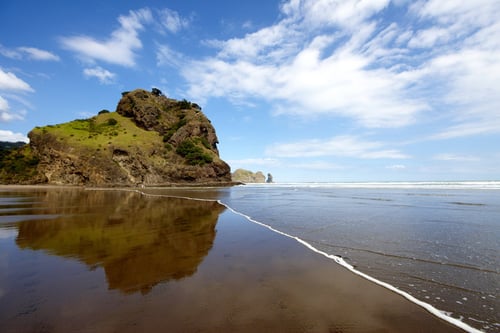 A vast sandy beach with rugged cliffs, crashing waves, and black sand stretching towards the horizon.
