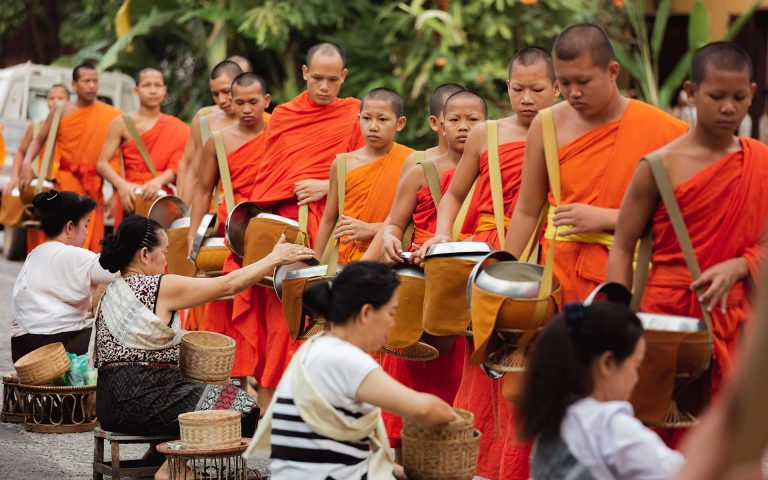 Buddhist monks in orange robe set out from their monasteries to receive offerings of food