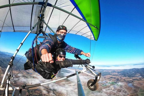 Two people hang gliding, soaring through the sky with the landscape far below, enjoying the freedom and exhilaration of flight.