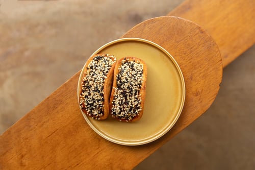 Two sesame-seed-covered pastries on a plate, placed on a wooden table.