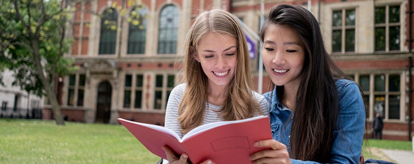 2 female university students looking at university guide book -SingSaver